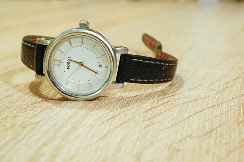 Fossil watch with leather belt on wooden background in soft focus